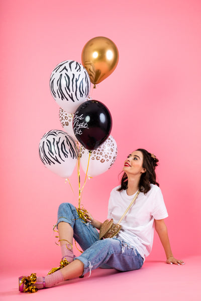 Gold, black and white balloons being held by a girl sitting on floor.