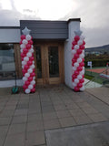 Red and white balloon columns on metal stands at a tennis club event.