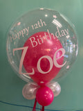 Pink personalised clear balloon against green background.