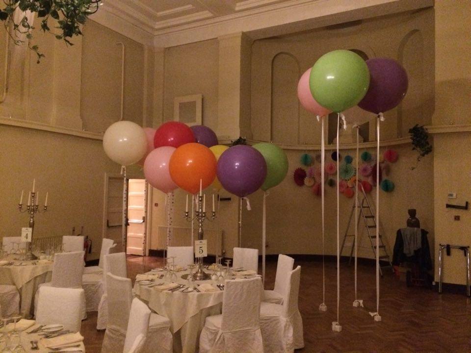 Different coloured large balloons floating from floor beside banquet table.