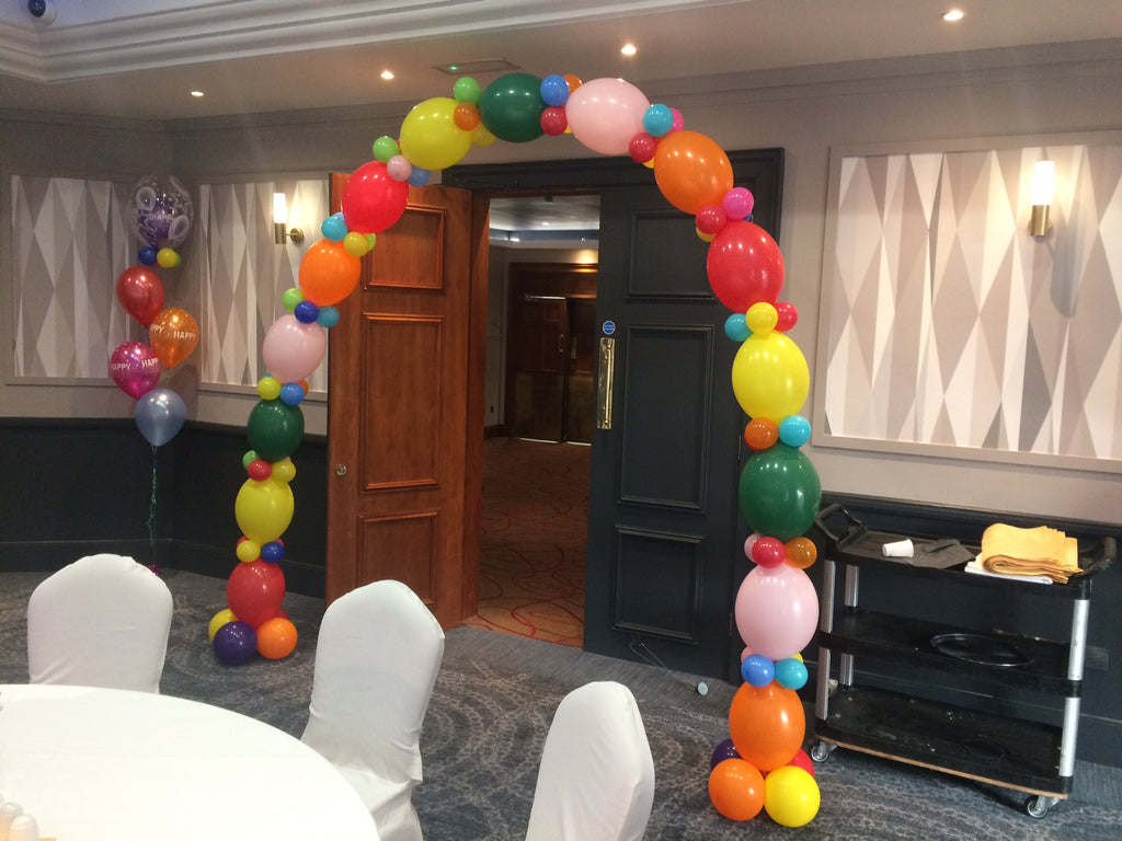 Large multicolour balloon arch over doorway  with balloon bouquet in corner of room.