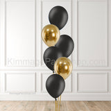 Black and gold balloons against a brick wall background.
