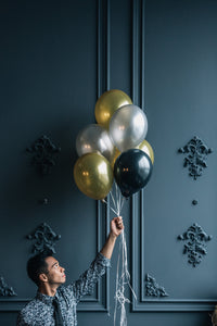 Man holding helium filled gold, silver and black balloons.