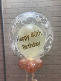 Ivory and rose gold coloured personalised 'happy birthday' balloon against brick wall.