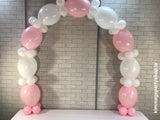 White and baby pink balloon arch on table.
